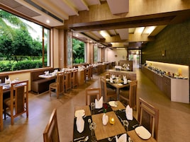 Un restaurante con varias mesas y cabinas, amplios ventanales que ofrecen vistas a zonas verdes, y un mostrador de buffet con diversos alimentos.