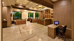 A modern reception area with a wooden reception desk, a computer, and a seating area with a patterned rug. - Sarovar Portico Gir (Mendarda)