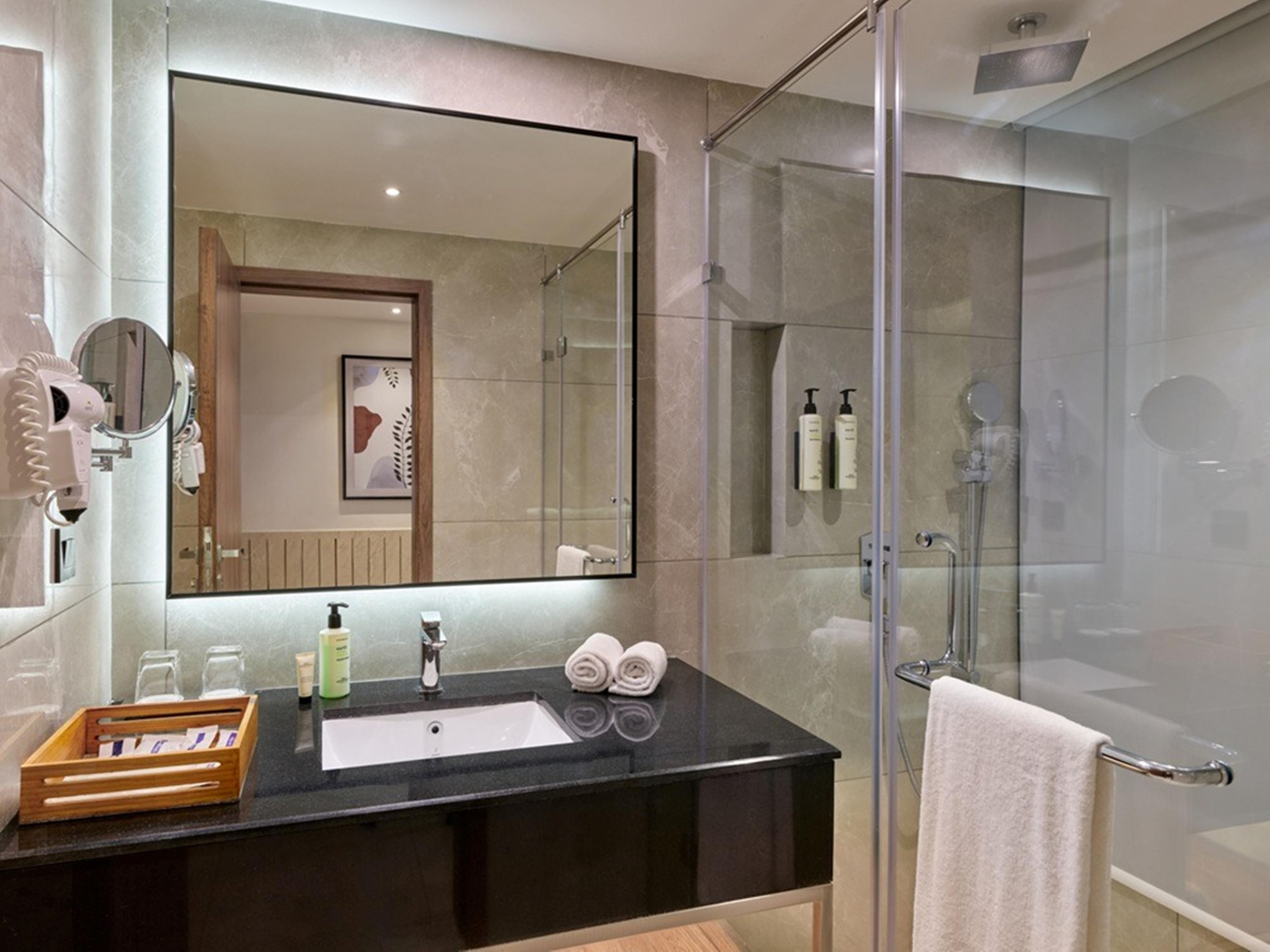 A modern bathroom with a glass-enclosed shower, a large mirror, and a black countertop with toiletries.