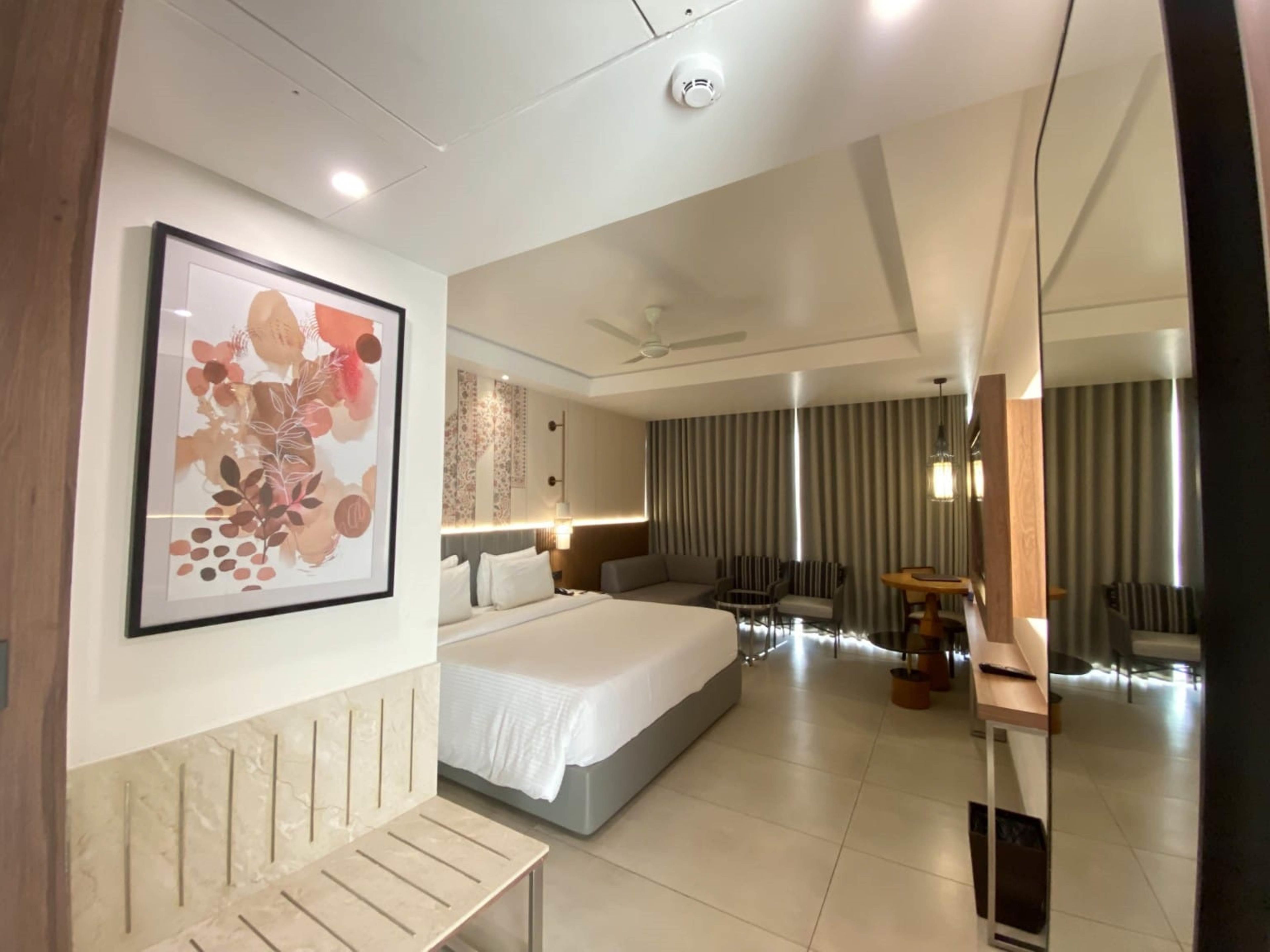 Quarto de hotel moderno com uma cama grande, uma escrivaninha, uma cadeira, um espelho e um ventilador de teto.