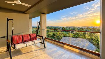 Un balcon avec un fauteuil suspendu, un ventilateur de plafond et une vue sur un paysage au coucher du soleil.