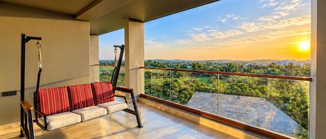 Un balcon avec un fauteuil suspendu, un ventilateur de plafond et une vue sur un paysage au coucher du soleil.