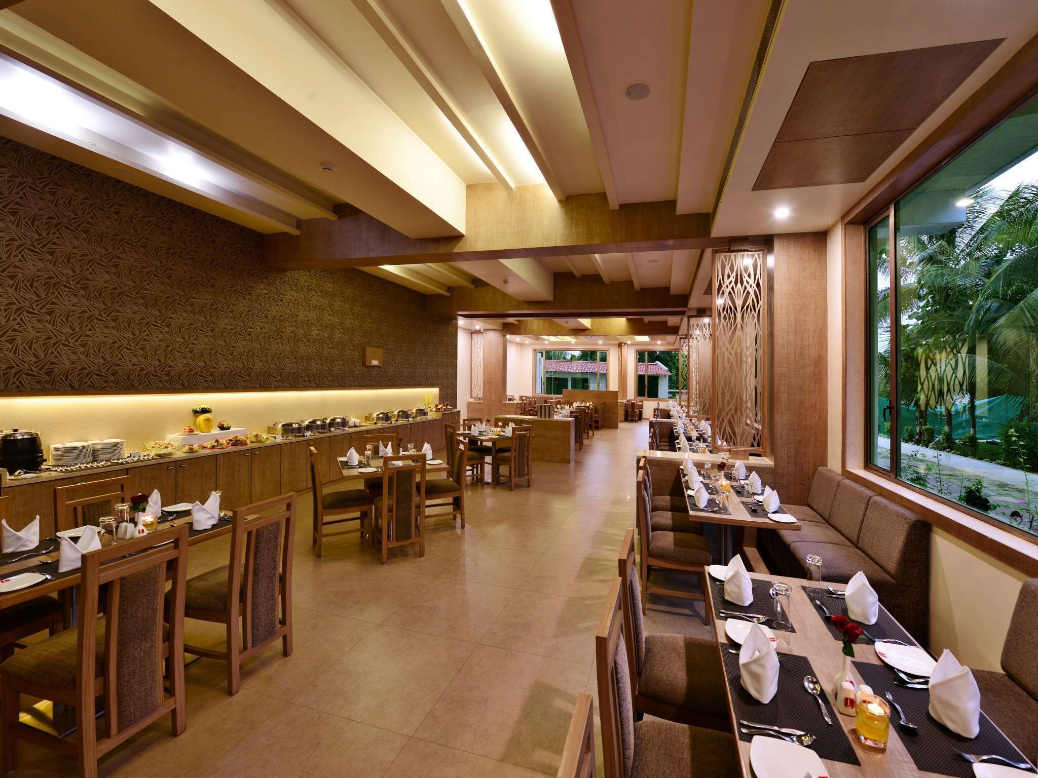 A restaurant with multiple dining areas, including a buffet and booths, with a view of greenery outside.