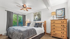 A bedroom with a large bed, a ceiling fan, a dresser, and a window with curtains. - Private Shuttle in Winter, Free Bus Route, Convenient Location + Hot Tub & Pool (Steamboat Springs)