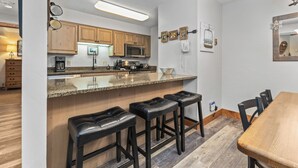 A modern kitchen with wooden cabinets, a granite countertop, and a bar area with stools. - Private Shuttle in Winter, Free Bus Route, Convenient Location + Hot Tub & Pool (Steamboat Springs)
