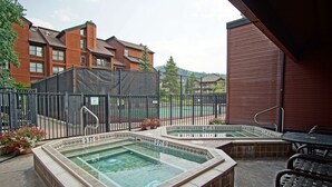 A rooftop patio with two hot tubs, a tennis court in the background, and a brick building. - Private Shuttle in Winter, Free Bus Route, Convenient Location + Hot Tub & Pool (Steamboat Springs)