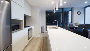 A modern kitchen with built-in appliances, a large island, and a dining area with a view. - Sydney CBD 2-Bedroom Apartment with Hyde Park Views - Sleeps 6 (Sydney)