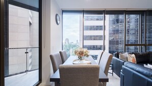 A modern living room with a dining table, a sofa, and large windows offering a city view. - Sydney CBD 2-Bedroom Apartment with Hyde Park Views - Sleeps 6 (Sydney)