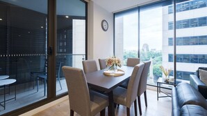 A modern dining area with a table and chairs, large windows with a city view, and a clock on the wall. - Sydney CBD 2-Bedroom Apartment with Hyde Park Views - Sleeps 6 (Sydney)