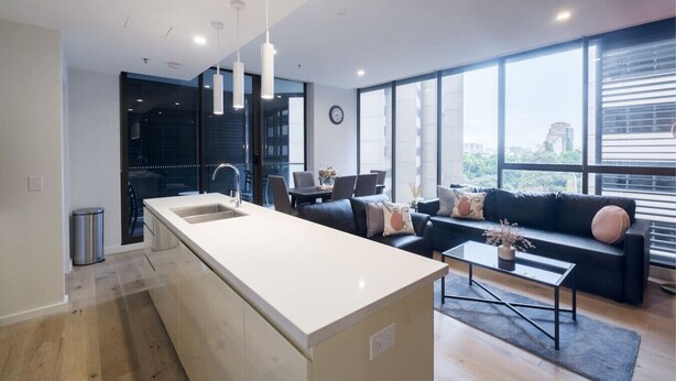 A modern kitchen with a large island, a dining area with a table and chairs, and a living room with a sofa and a coffee table. - Sydney CBD 2-Bedroom Apartment with Hyde Park Views - Sleeps 6 (Sydney)