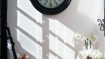 A wall-mounted clock, a wooden bench, a white orchid vase, and a metal umbrella stand.