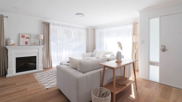 Uma sala de estar moderna com lareira, sofá, mesa lateral de madeira e uma janela grande com cortinas.