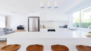 Uma cozinha moderna com armários brancos, uma ilha grande com banquetas e uma geladeira embutida.