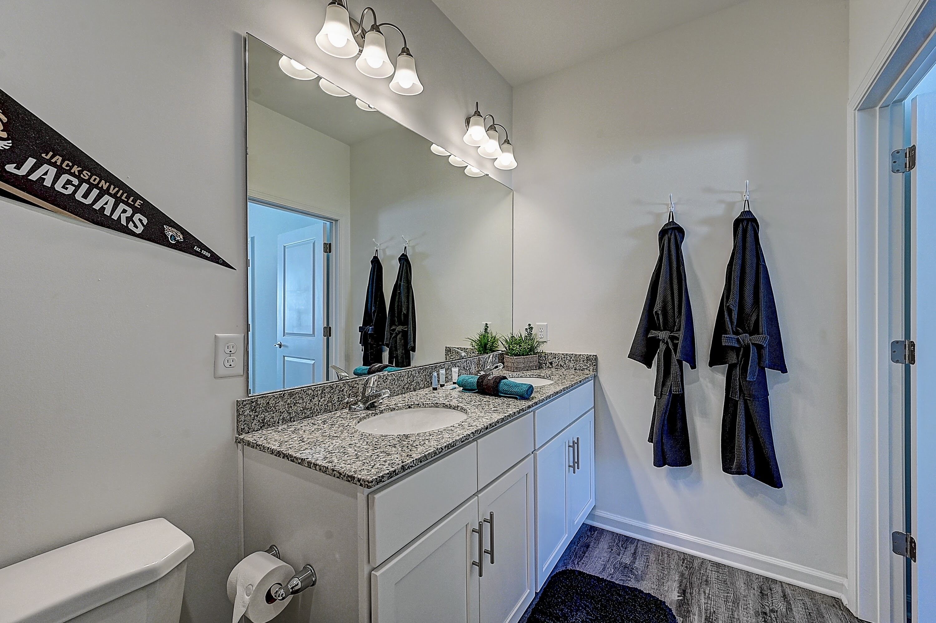 Une salle de bain avec un meuble-lavabo à deux vasques, un grand miroir et des serviettes suspendues à des crochets.