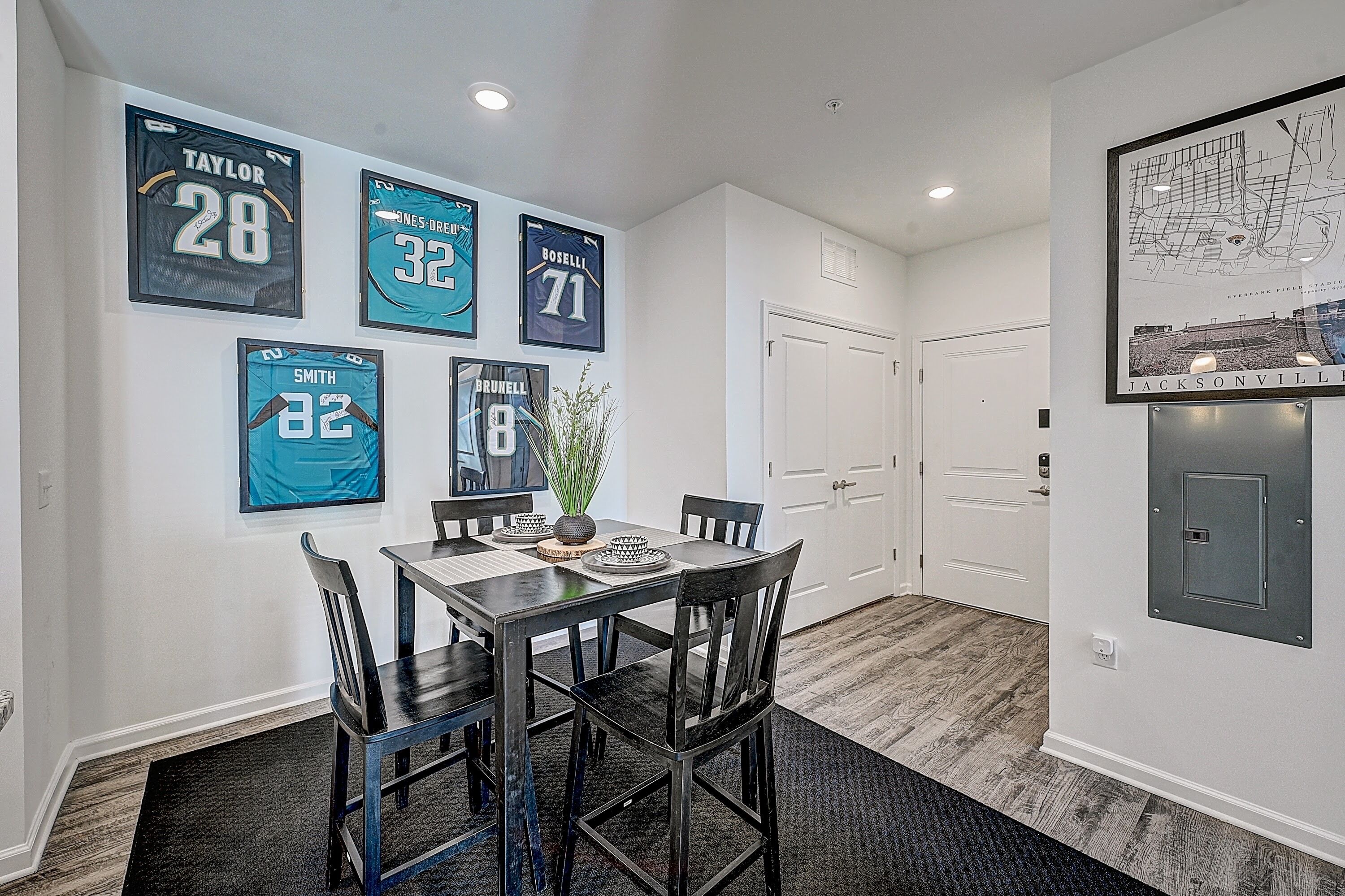 A dining area with a table and chairs, a potted plant, and sports jerseys on the wall.