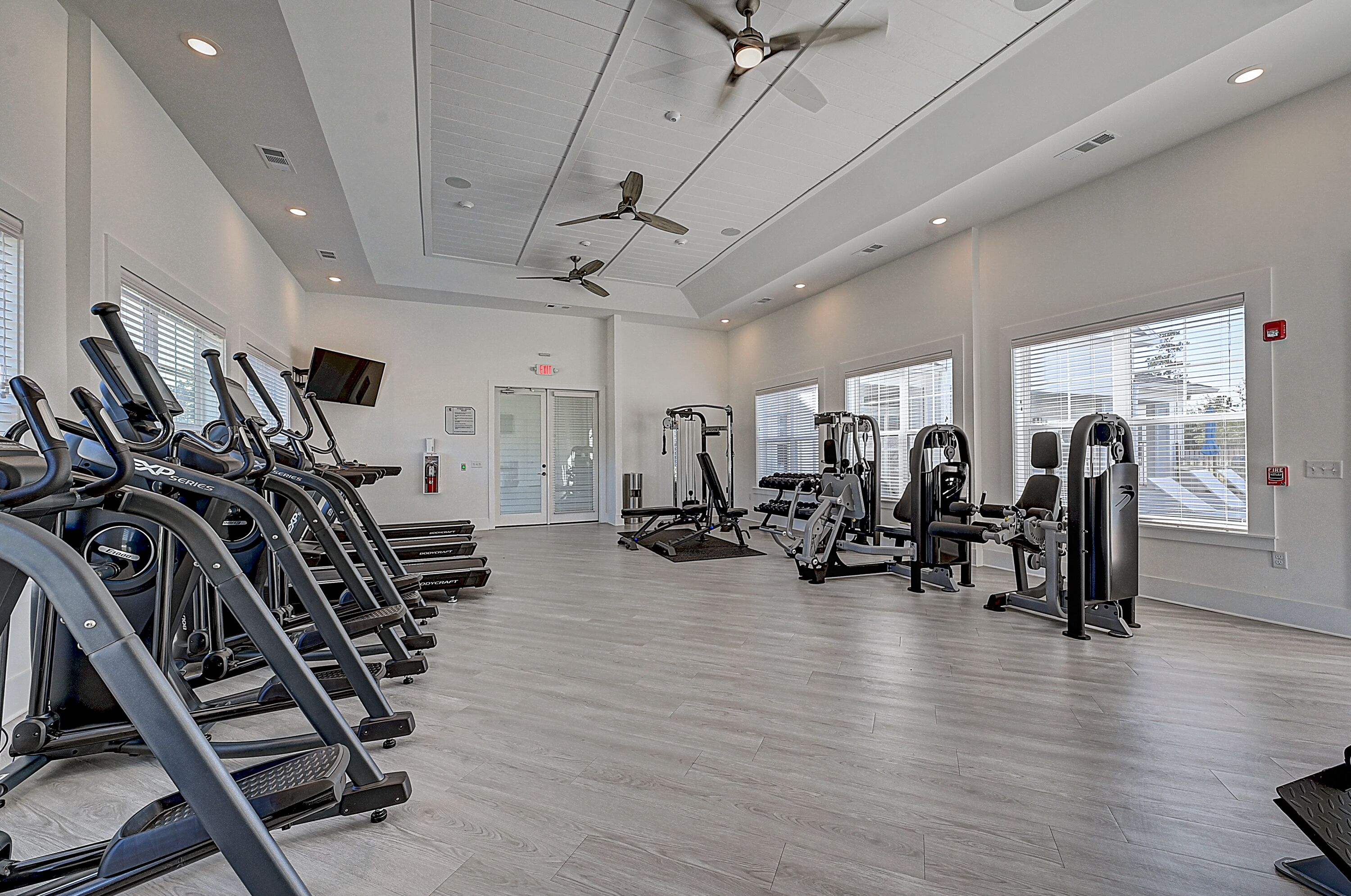 Une salle de sport équipée de tapis de course, d’appareils de musculation et de ventilateurs au plafond.