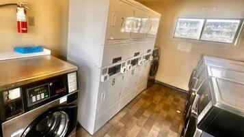 A laundry room with stacked washers and dryers, a fire extinguisher, and a view of the outside through a window.