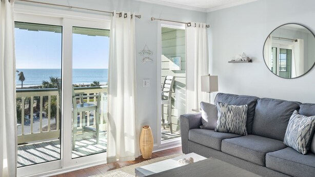 A modern living room with a grey sofa, a round mirror, and a view of the ocean through large sliding doors. - 3rd Floor Condo w/Amazing Ocean View! Pool & Pier Access! *Unit 328* (Isle Of Palms)