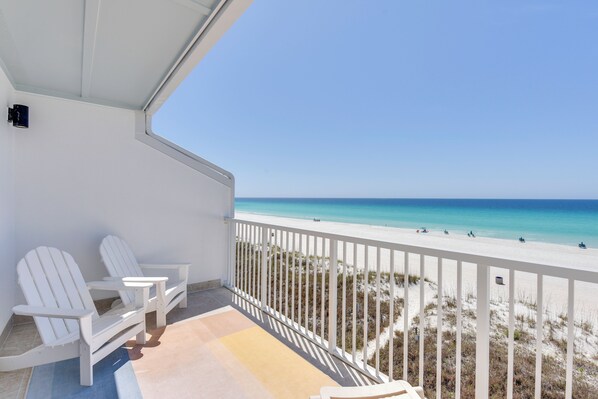 Ein Balkon mit weißen Adirondack-Stühlen, einem kleinen Tisch und Blick auf den Strand.