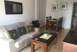 Een woonkamer met een bank, een salontafel, een eettafel met stoelen, een spiegel en wanddecoratie.