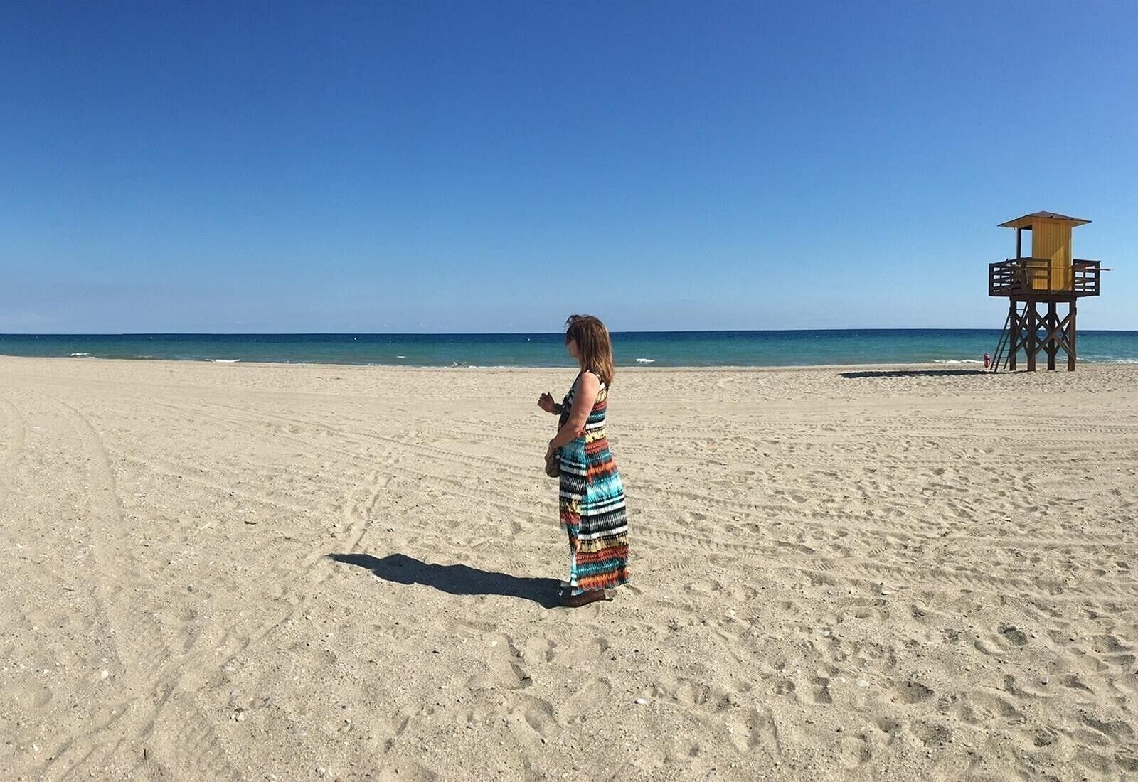 A beach with a lifeguard tower and a person in a patterned dress.