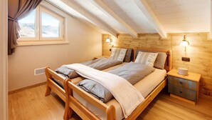 Un dormitorio con cama de madera, una mesita de noche, una ventana con cortinas y una lámpara fijada a la pared.