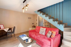 A living room with a red sofa, a wooden coffee table, a chair, and a staircase with blue walls.