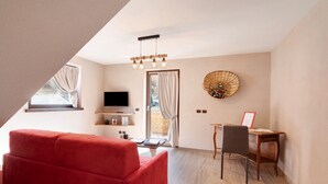 Una sala de estar moderna con un sofá rojo, un escritorio de madera, un televisor y un ventilador decorativo.
