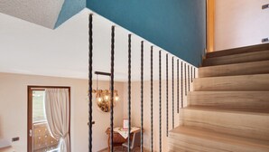 Una escalera con escalones de madera y barandillas negras, un comedor con mesa y sillas, y una vista a través de un ventanal.