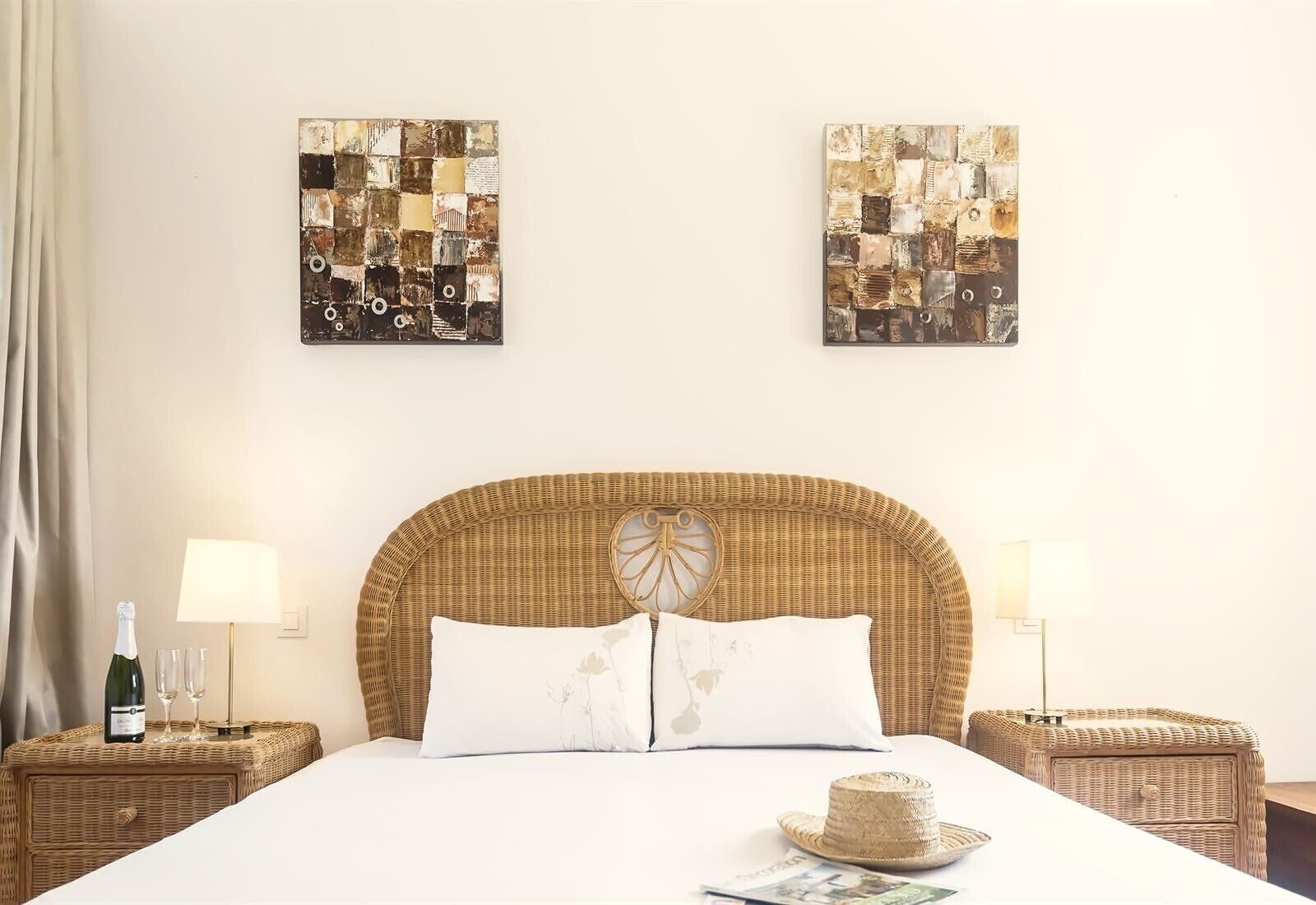 Habitación de hotel con una cama grande, dos mesitas de noche con lámparas, un cabecero de mimbre y dos obras de arte colgadas en la pared.