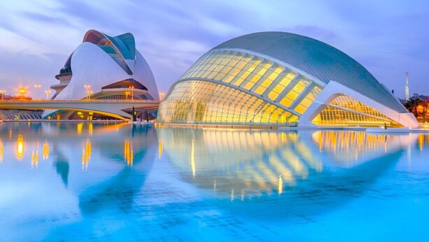 Un bâtiment d’architecture moderne au design original, caract érisé par des lignes courbes, une grande piscine aux reflets argentés à l’avant et un ciel dégagé.