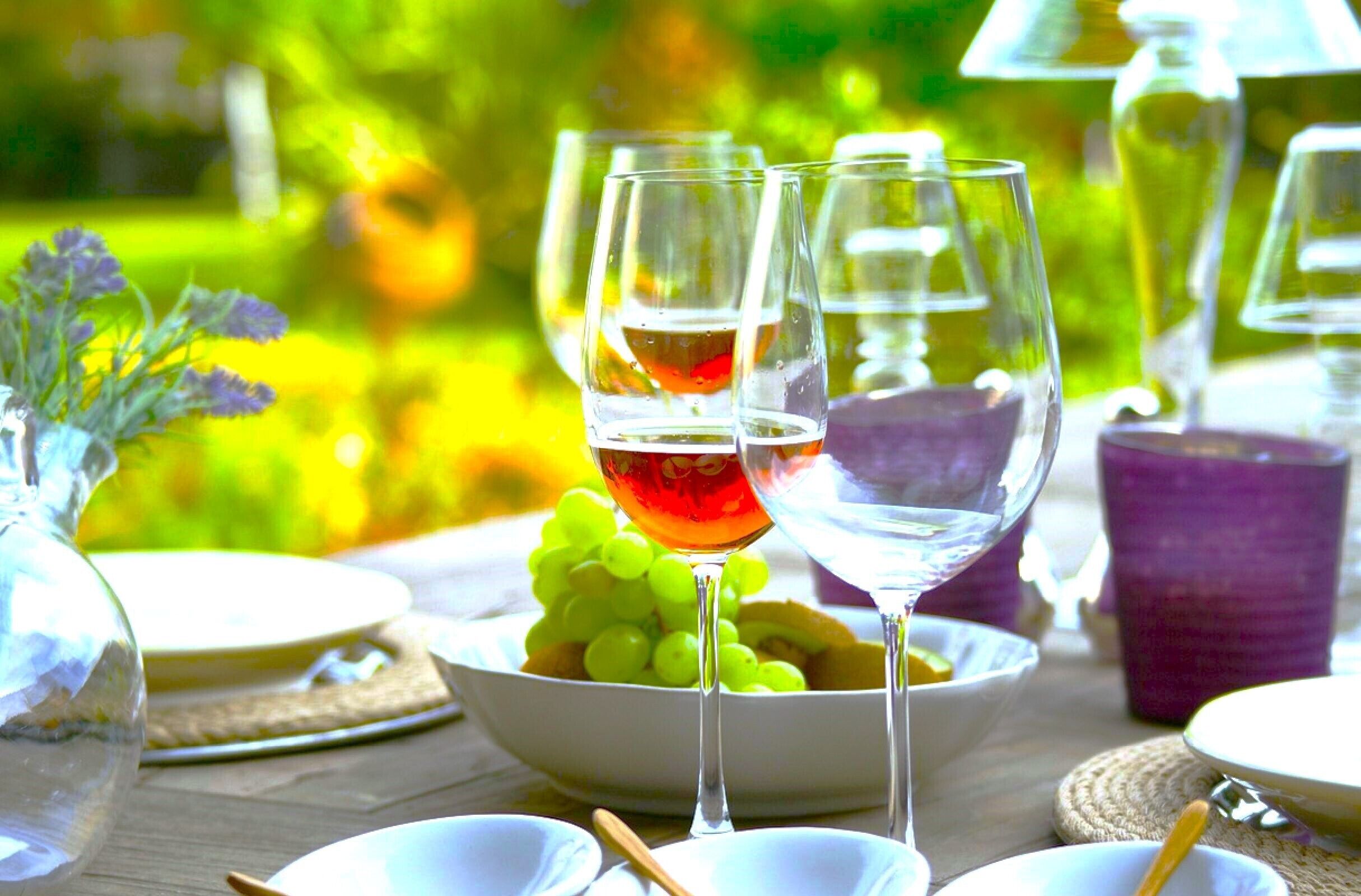 Una mesa con copas de vino, un bol de uvas y un jarrón con flores.