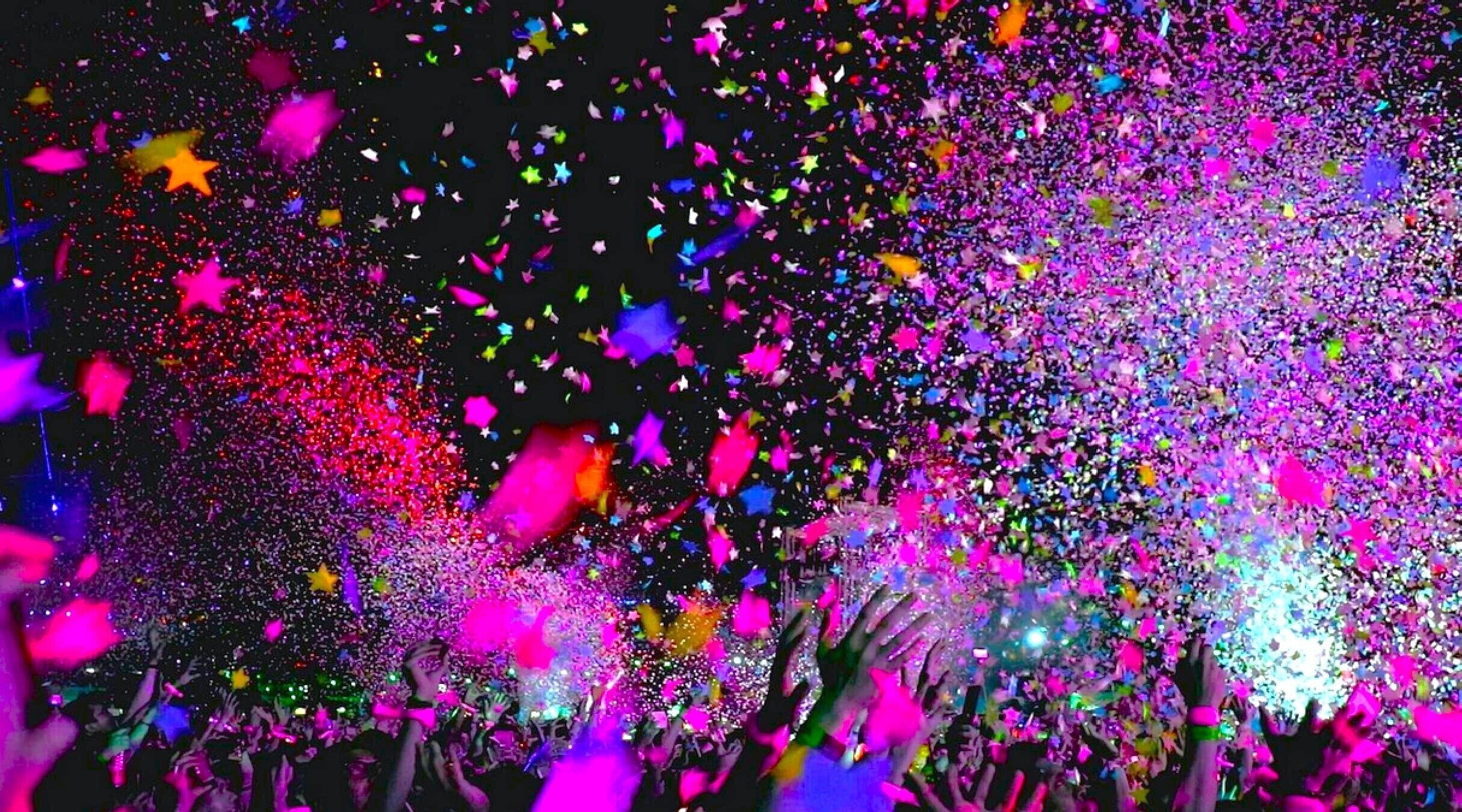A crowd at a concert with colorful lights and confetti.