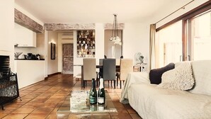 Un salon avec un canapé, une table basse sur laquelle sont posées des bouteilles, un coin repas avec des chaises et une cuisine avec un comptoir.