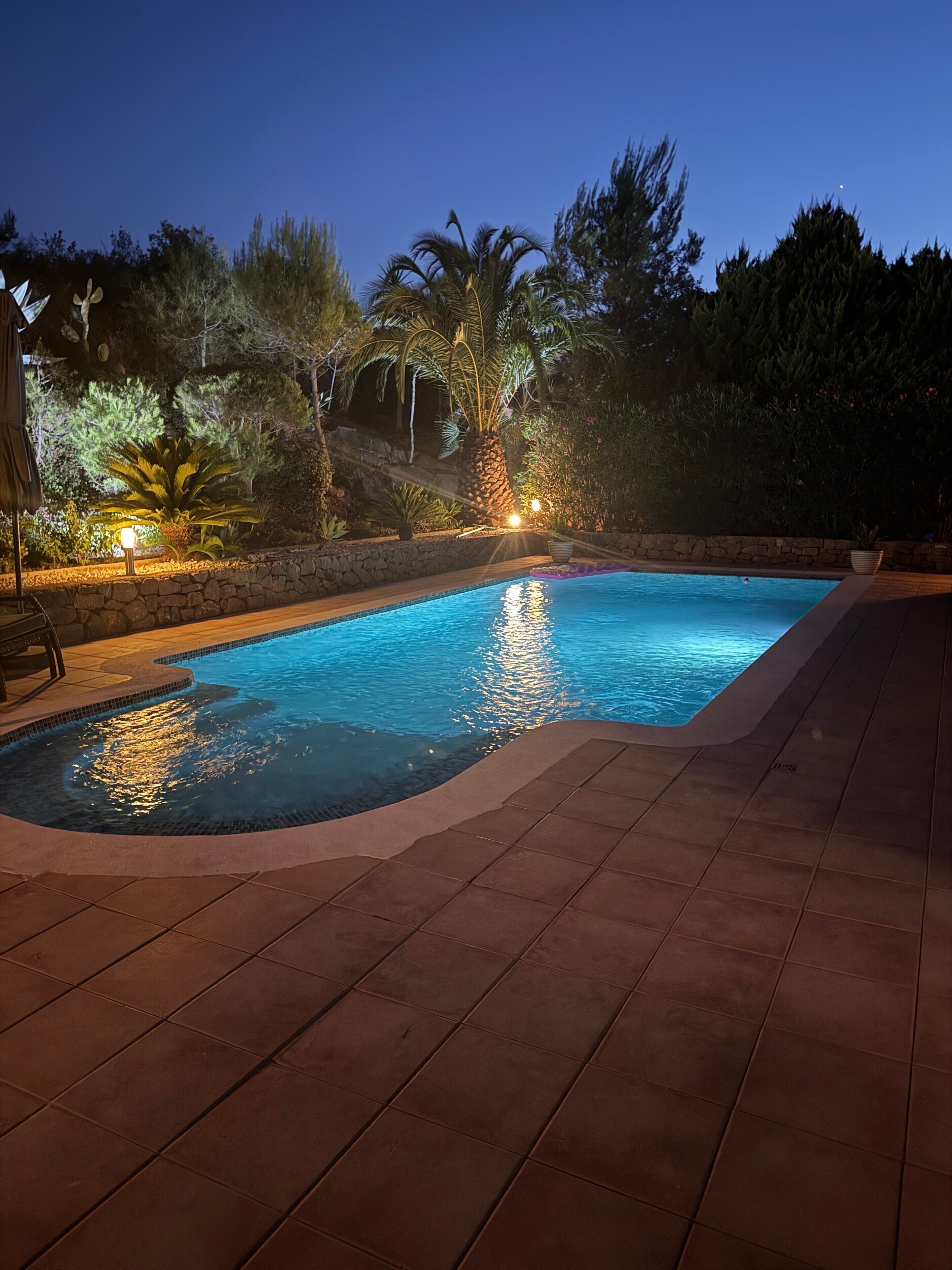 Une piscine bordée de pierres et dotée d’une terrasse carrelée.
