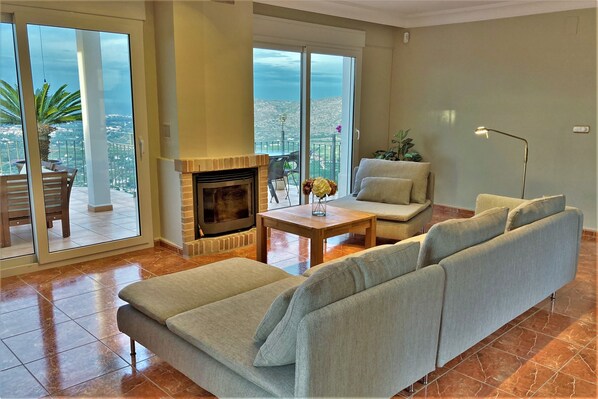 A living room with a sofa, a small table, a fireplace, and a balcony with a view.