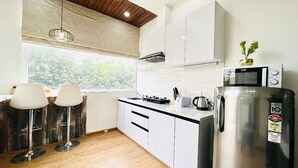 Une cuisine moderne avec des meubles blancs, un réfrigérateur en acier inoxydable et une fenêtre donnant sur un paysage verdoyant.