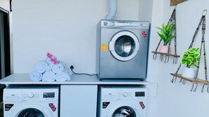 Deux machines à laver à chargement frontal, l’une placée sur l’autre, avec une pile de serviettes pliées et des fleurs roses sur une table blanche.