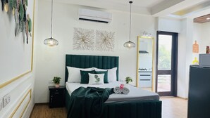 Une chambre à coucher avec un lit recouvert d’un tissu vert, une table de chevet ornée d’une plante et un grand miroir accroché au mur.