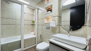 Une salle de bain moderne avec une baignoire, des toilettes et un lavabo. On y trouve des étagères ornées de fleurs et un miroir au-dessus du lavabo.