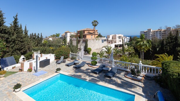 Une piscine avec des chaises longues, une clôture blanche et des bâtiments en arrière-plan.