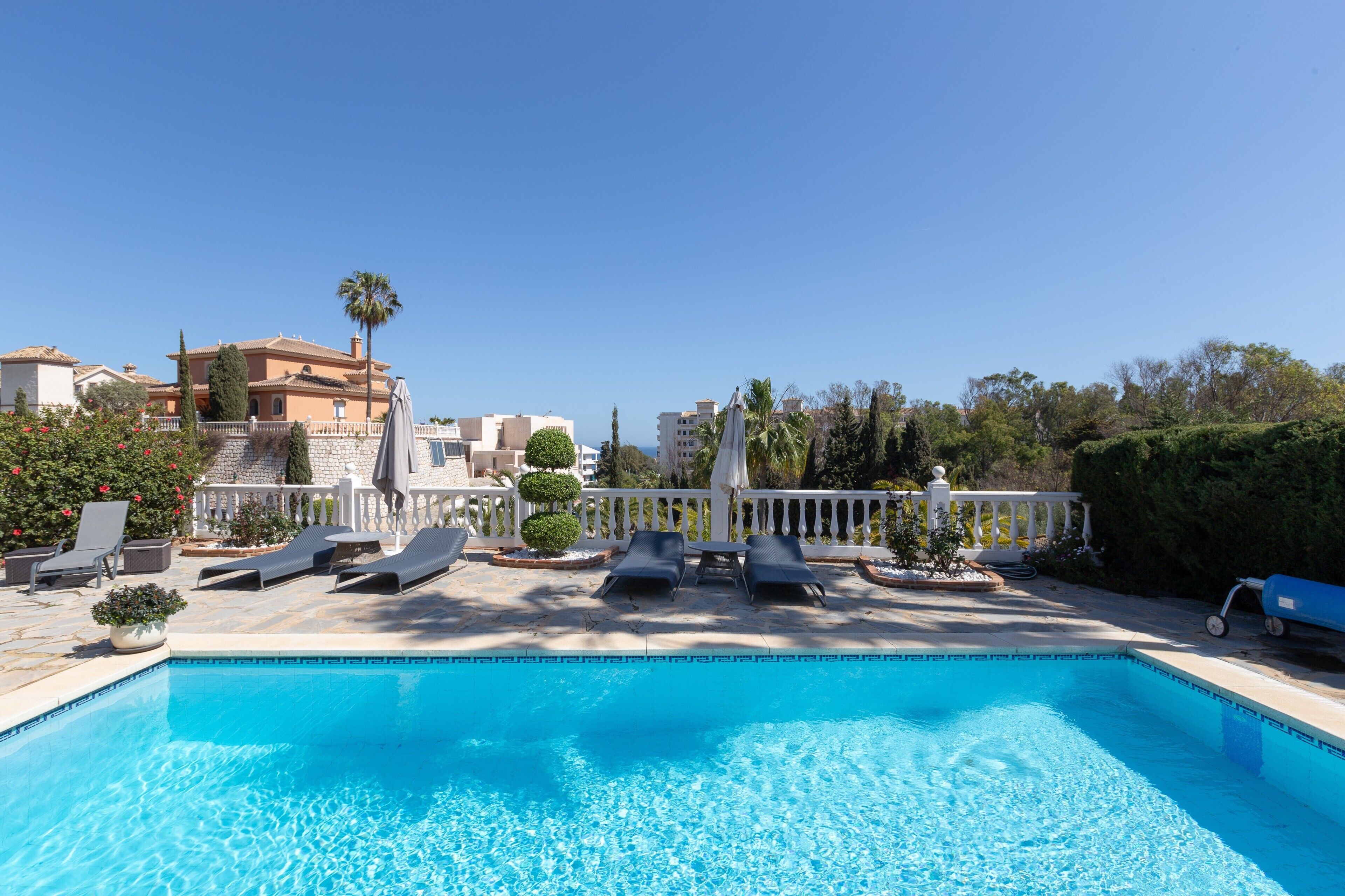 Una piscina con sillas de descanso, una cerca blanca y un edificio al fondo.