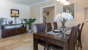 Un coin repas avec une table en verre, des chaises marron, un vase de fleurs et une lampe.