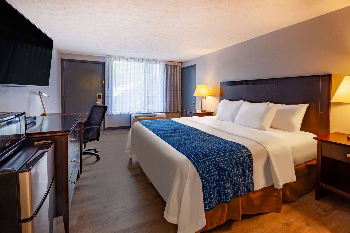 A hotel room with a bed, desk, chair, TV, and lamps.
