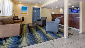 A hotel lobby with a reception desk, a seating area with a sofa and armchairs, a painting on the wall, and a door. - Travelodge By Wyndham Charles Town/Harpers Ferry (Charles Town)