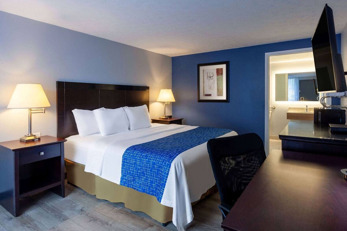 A hotel room with a bed, two bedside lamps, a desk with a computer, a chair, and a TV.