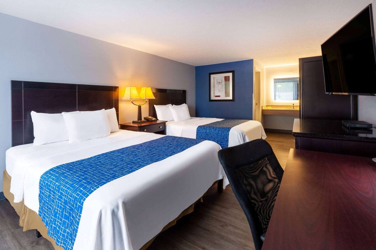A hotel room with two beds, a desk, a TV, and a bathroom visible through an open door.