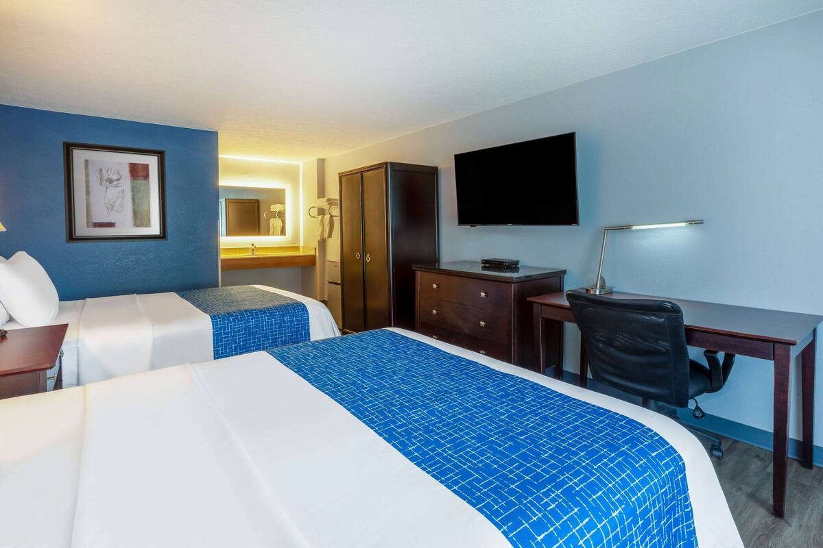 A hotel room with two beds, a desk, a chair, a television, and a wardrobe.
