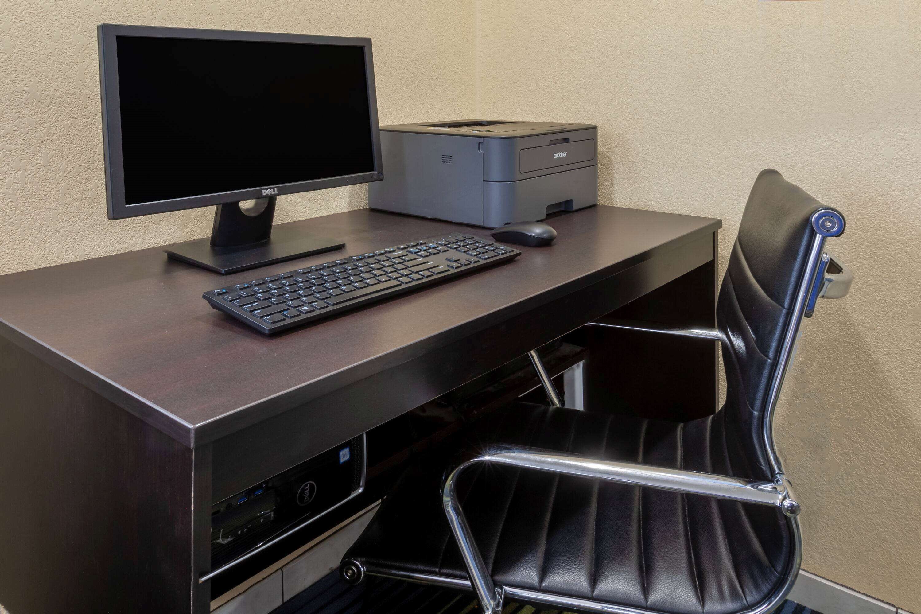 Ein dunkler Holztisch mit einem Dell-Monitor, einer Tastatur, einem Drucker und einem schwarzen Ledersessel.