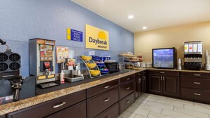 A breakfast area with a coffee machine, food display, and a TV screen. - Travelodge By Wyndham Charles Town/Harpers Ferry (Charles Town)